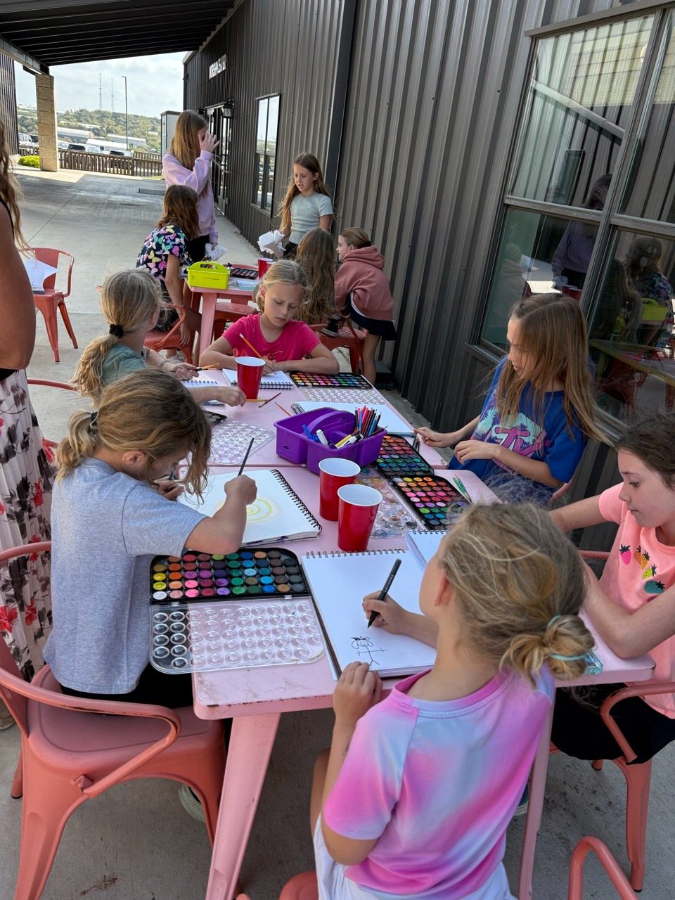 Children gathered around a table painting and drawing together outdoors