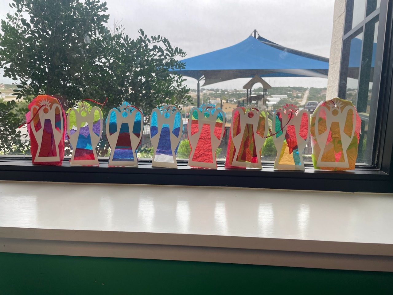 A row of tissue paper angel crafts lined up along a sunny windowsill