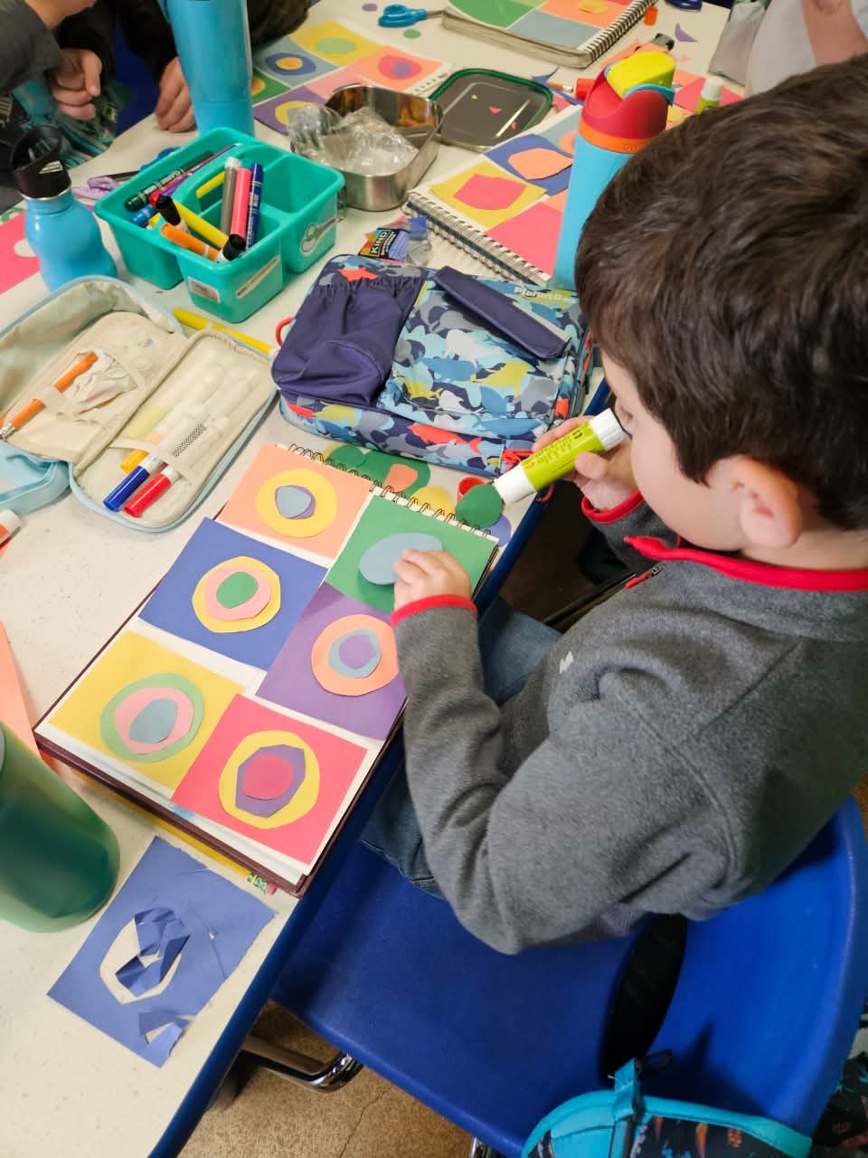 A child gluing colorful paper circles into a Kandinsky-inspired grid
