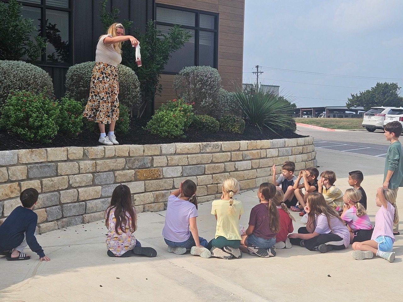 A teacher demonstrating an experiment from a stone ledge to children seated below