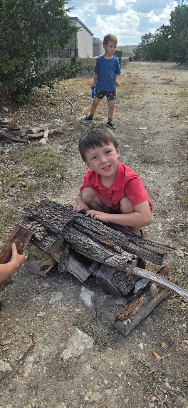 A child stacking bark and logs into a small shelter outdoors