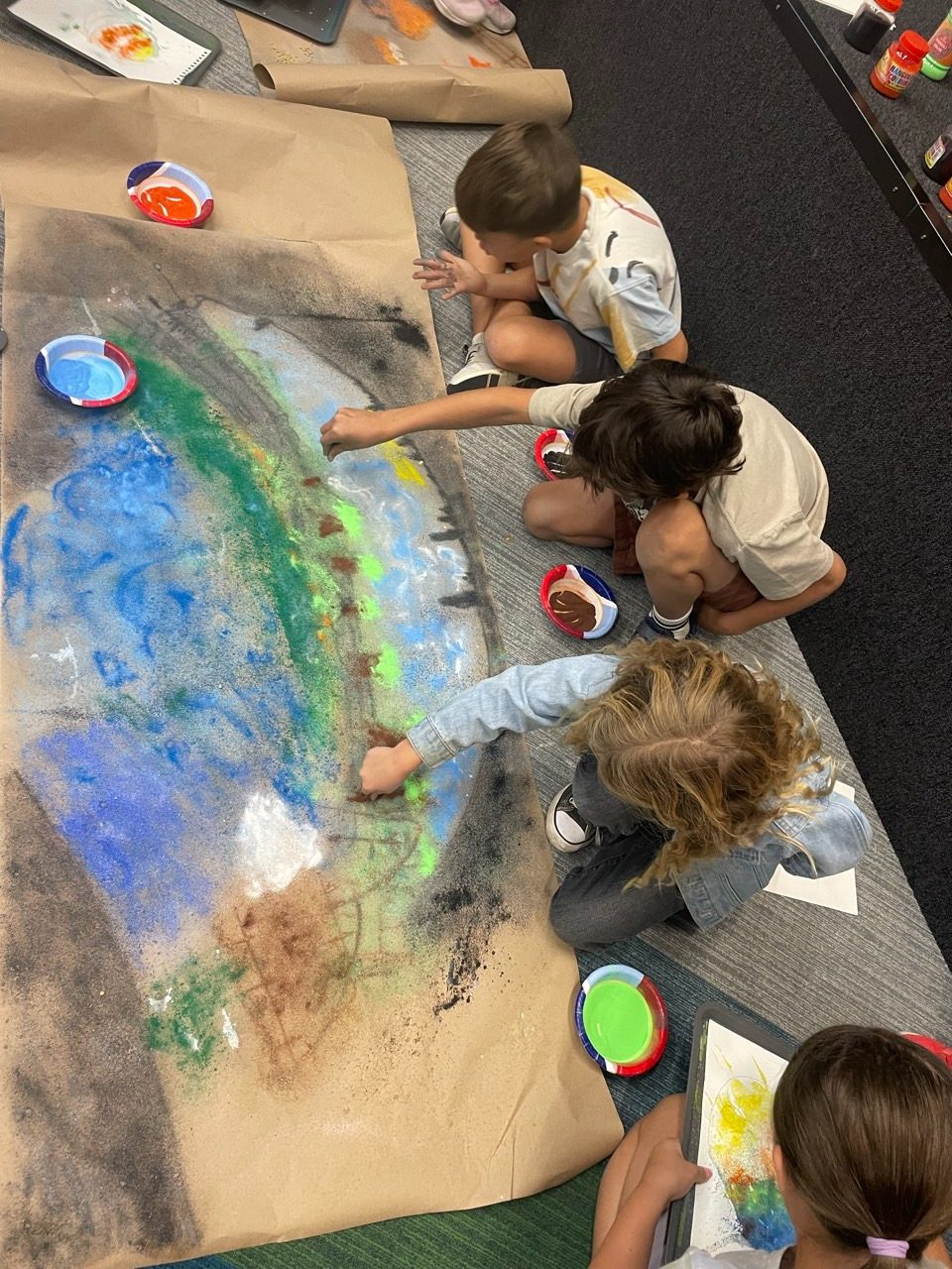Children painting a large collaborative mural on butcher paper on the floor