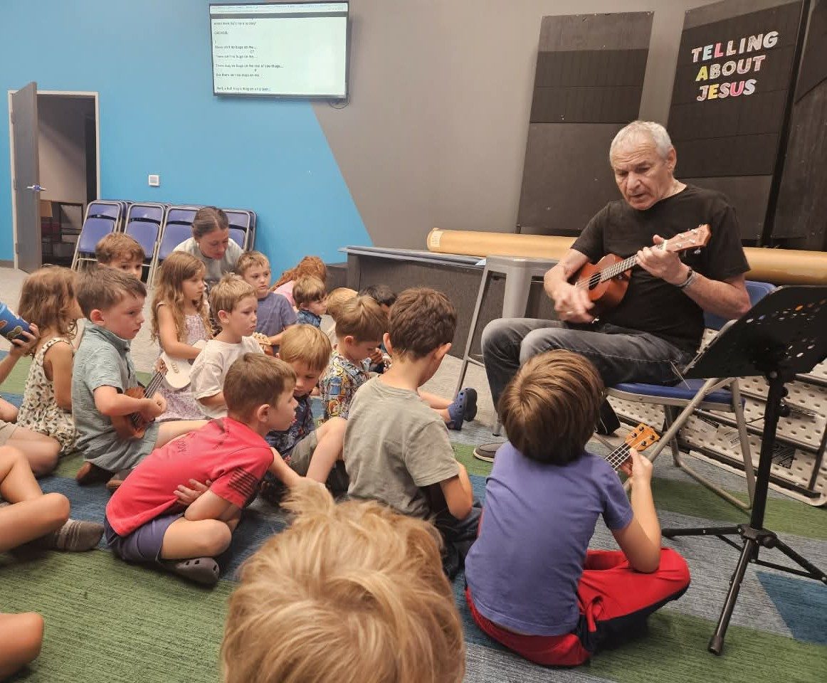 A guest musician playing ukulele for a group of children seated on the floor