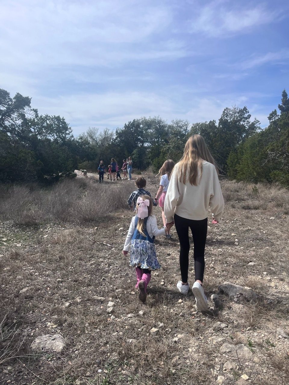 An older student leads younger children by the hand on a nature walk through the Hill Country
